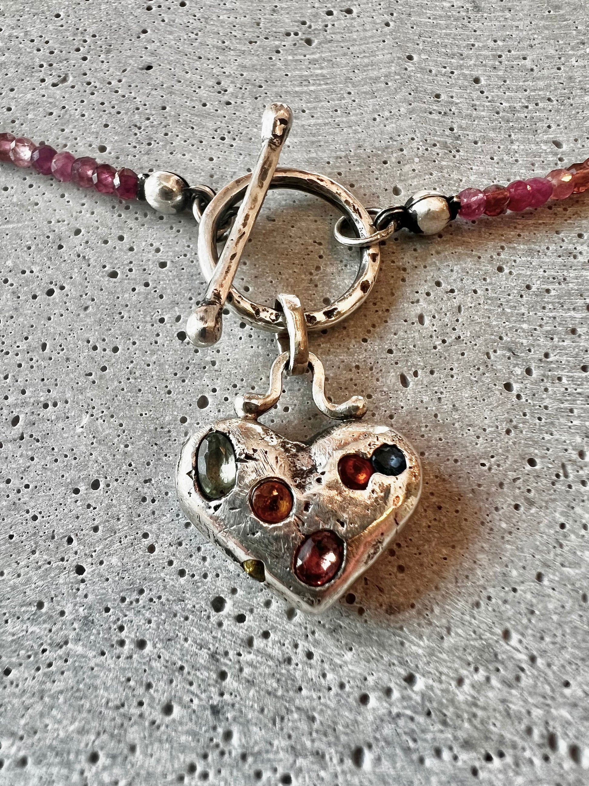 Discover our Colorful Heart Sapphire Necklace – a 15mm heart pendant adorned with seven ethically sourced sapphires, each representing a chakra. Crafted from recycled sterling silver using sand casting technique. A harmonious blend of elegance and energy.